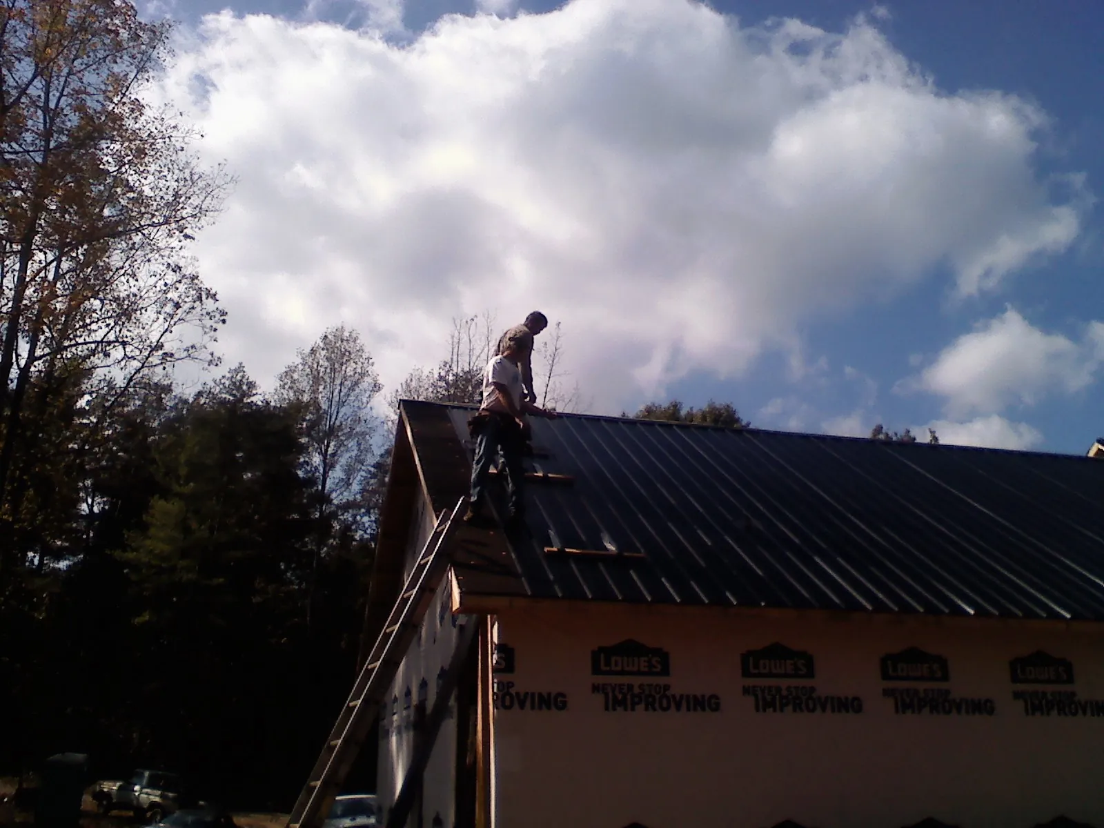 Roofer fastening dark metal panels high against a cloudy sky, from a Roof Inspection job in Dravosburg