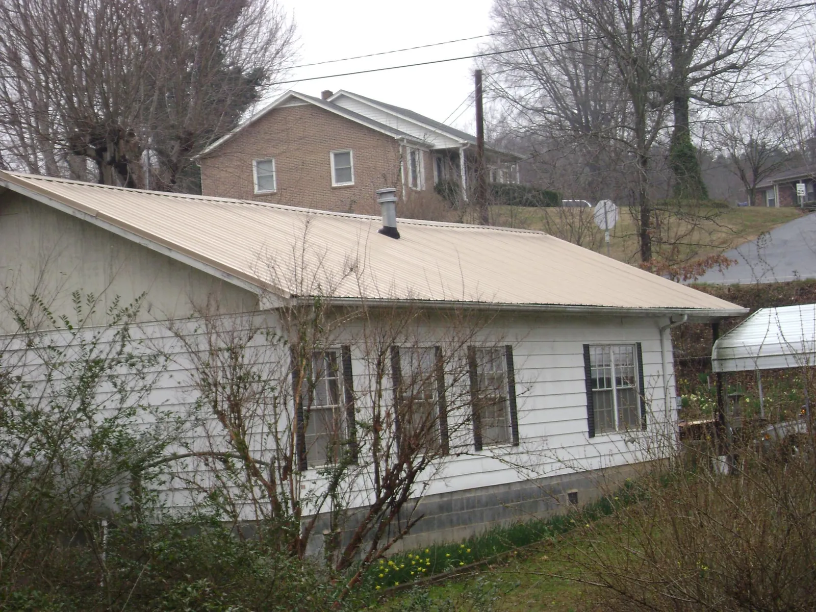 Tan metal roof on a white sided house set into a hillside — Commercial Roofing by Roofing Brothers in Dravosburg